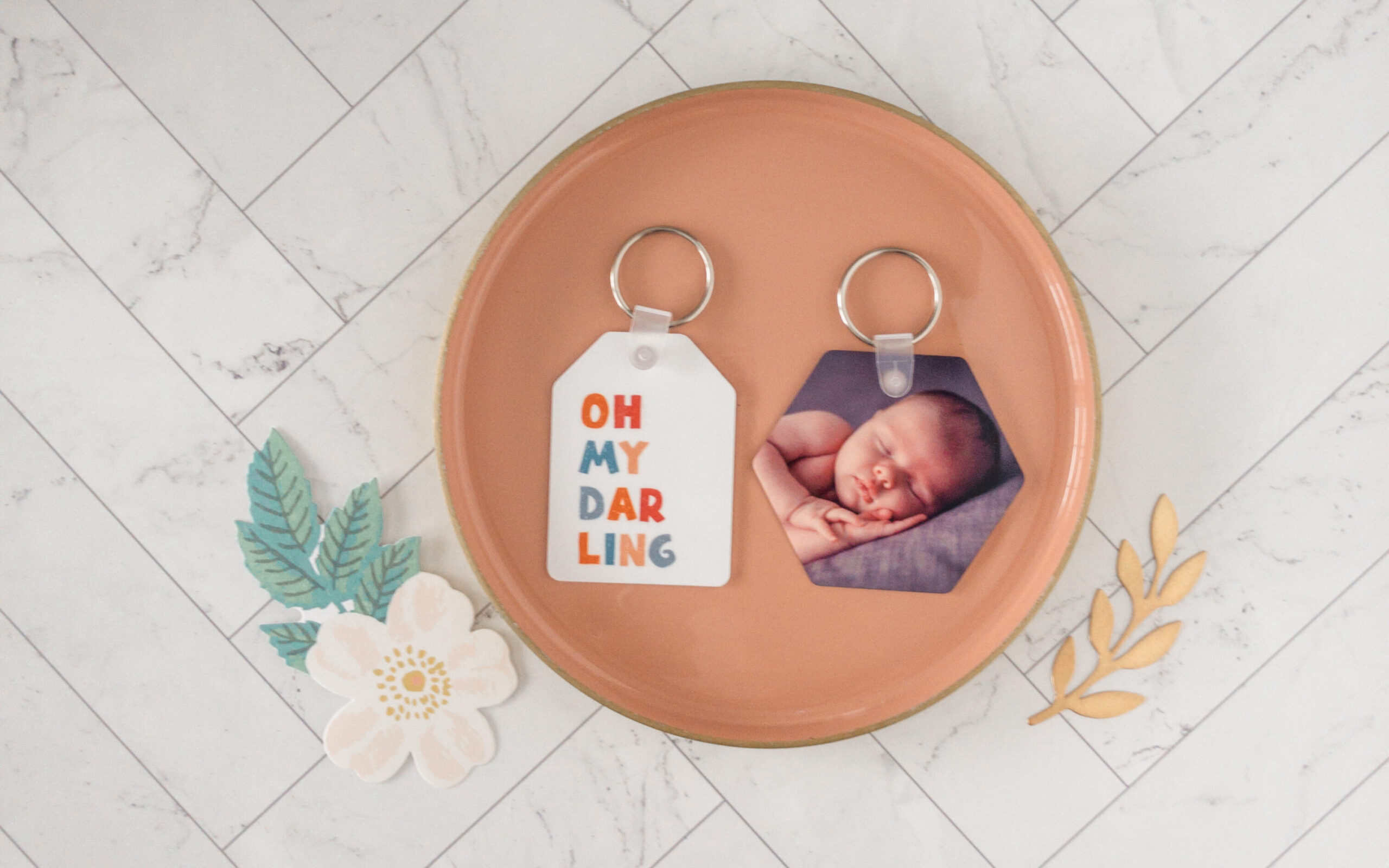 Two Unisub keychains one with a photo of a newborn and another with "oh my darling" printed on the other for a colorful suml